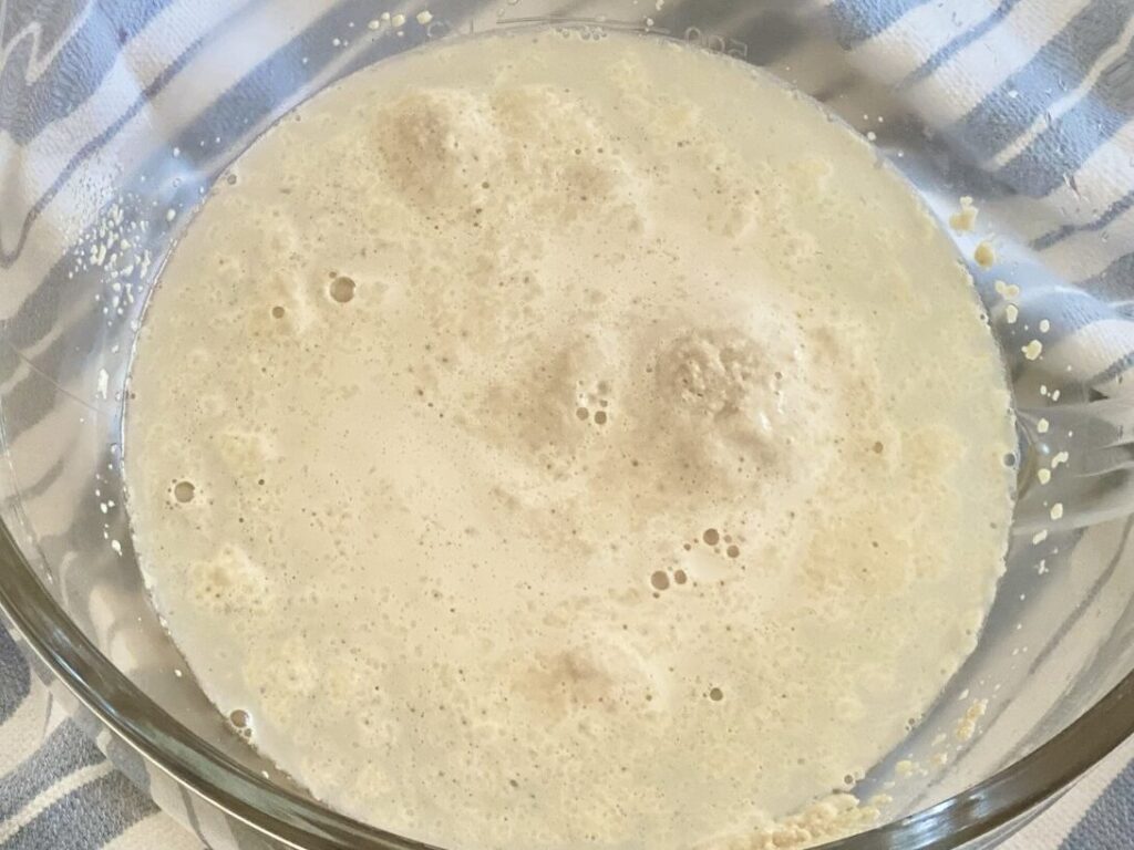 Close-up of yeast activating in warm water with bubbles forming, a crucial step in the homemade bread-making process.