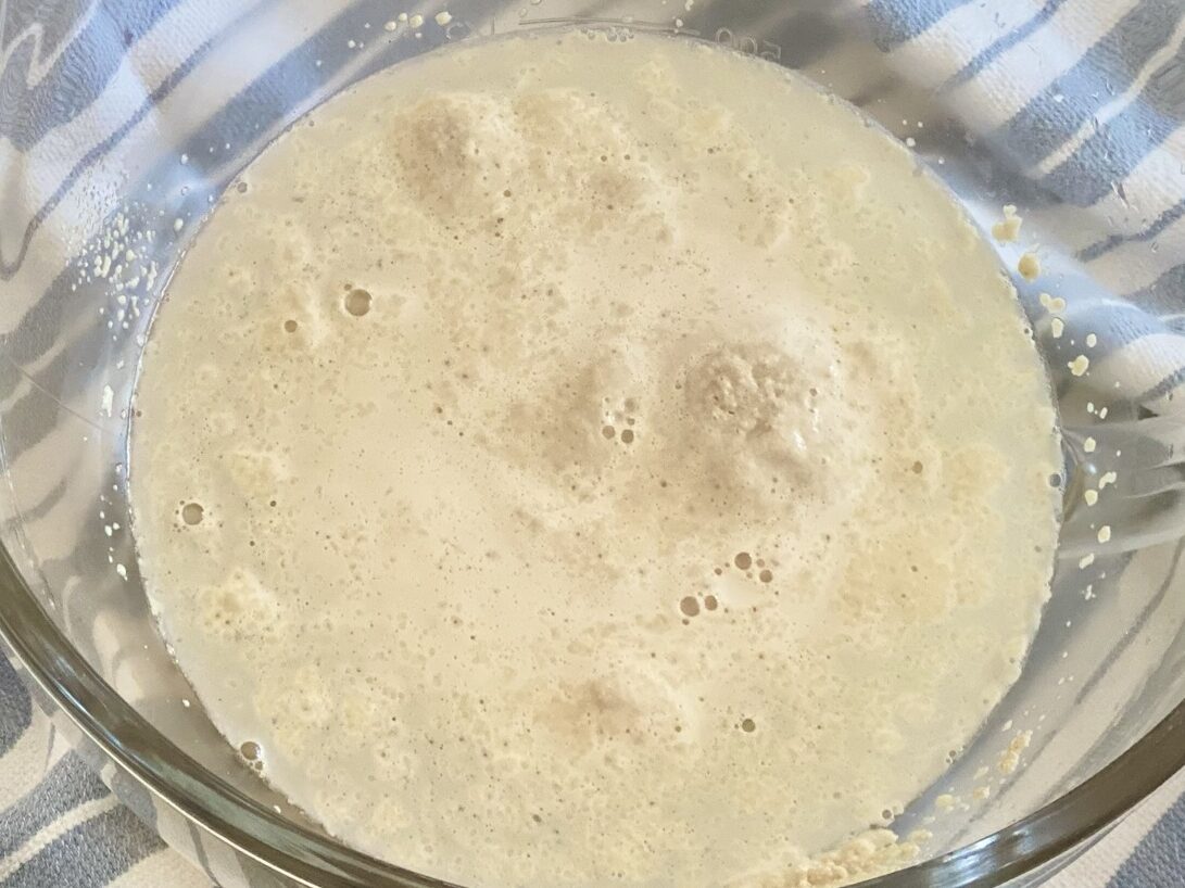 Close-up of yeast activating in warm water with bubbles forming, a crucial step in the homemade bread-making process.