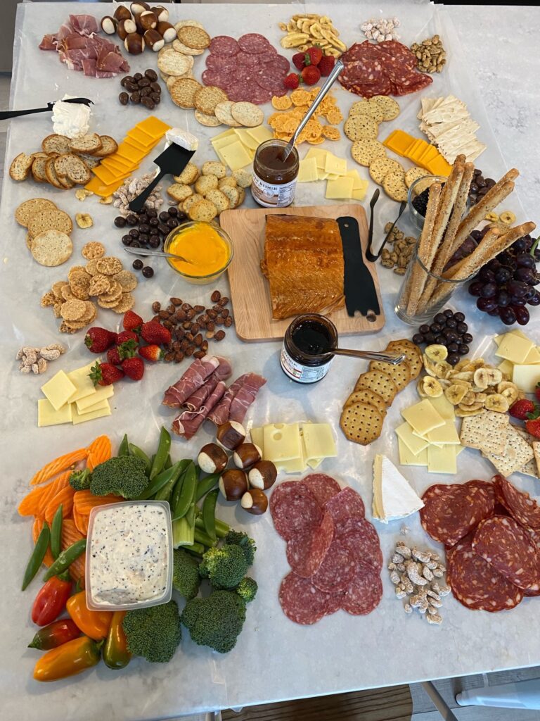 A wine tasting party setup showcasing a cheese and snack table with an assortment of cheeses, crackers, and fruits, paired with wine glasses.