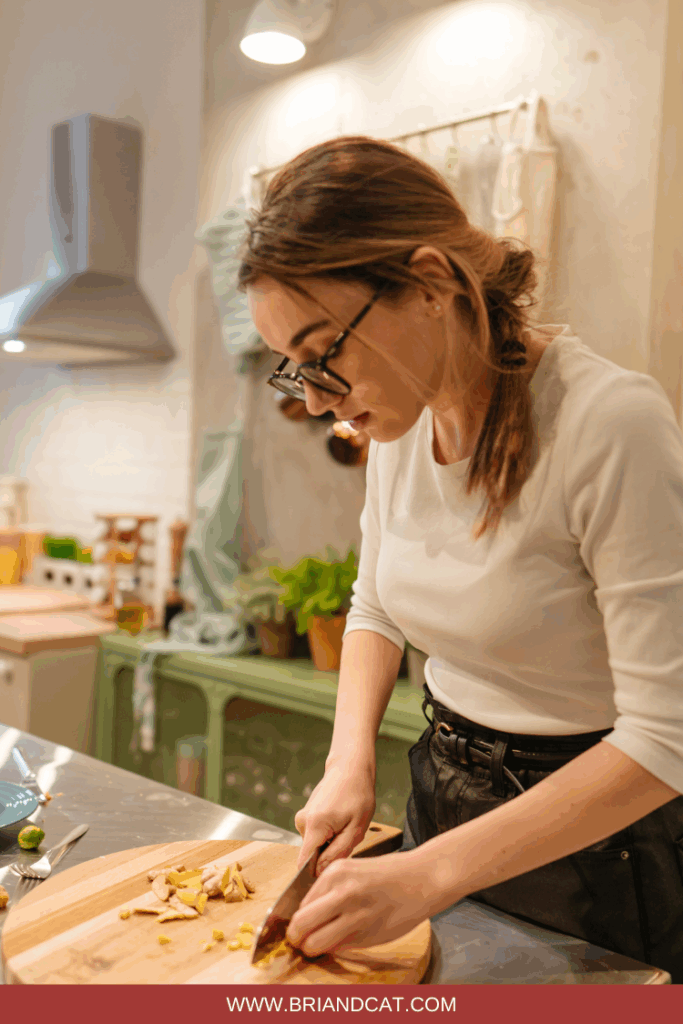 A person with glasses chopping food on a wooden cutting board in a well-lit kitchen.