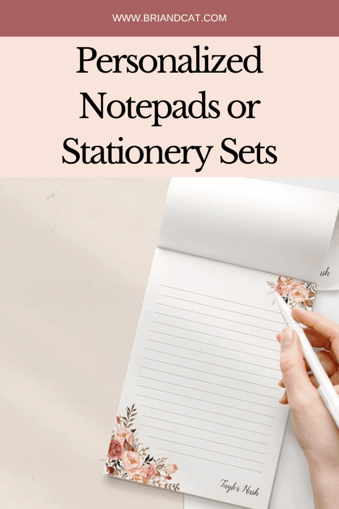 A hand holding a pen writing on a personalized notepad with floral designs and a name at the bottom.