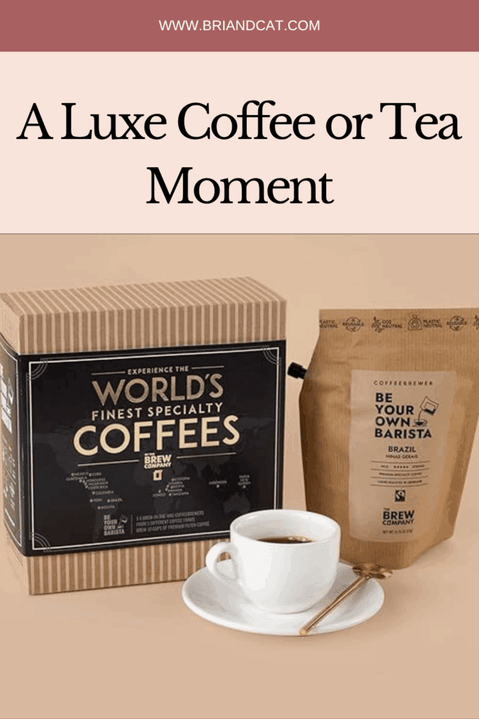 A coffee gift set featuring a box labeled 'World's Finest Specialty Coffees' and a bag of coffee labeled 'Be Your Own Barista' next to a white cup of coffee on a saucer with a spoon.