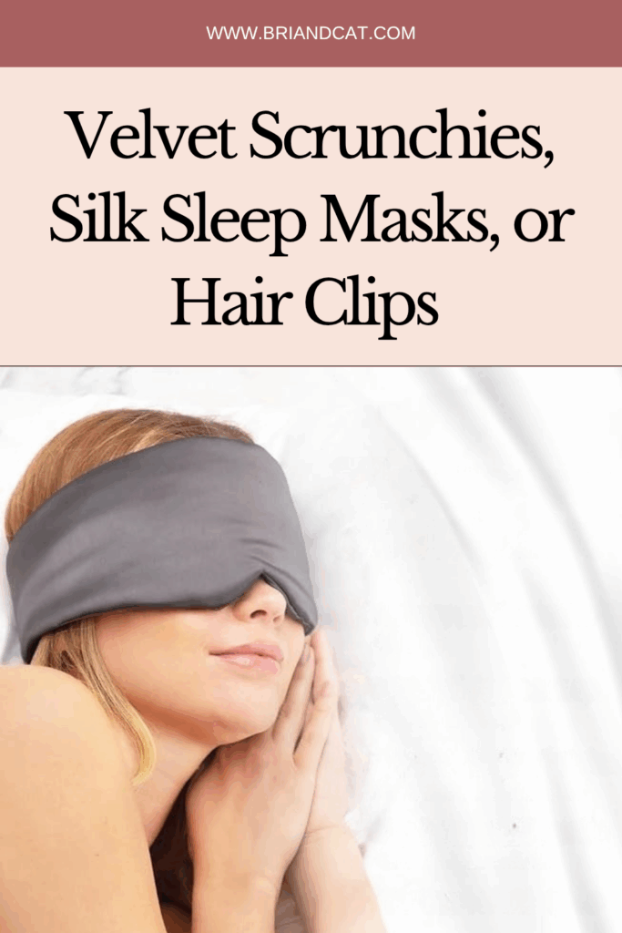 A woman relaxing in bed wearing a gray silk sleep mask, with her hair styled and resting her hands on her face.
