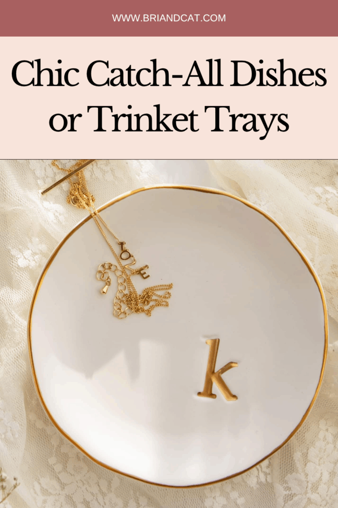 A chic white catch-all dish with a gold trim, featuring a small gold charm and an initial 'k' on it, set against a lace background.