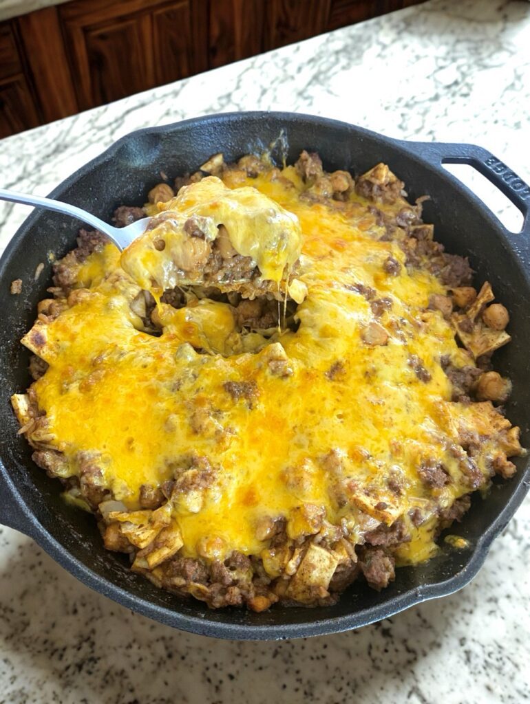 A cheesy, hearty Sloppy Enchilada Skillet filled with ground beef, chickpeas, and melted cheese in a cast-iron skillet.