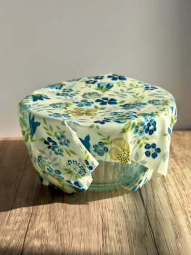 A glass bowl covered with a floral-patterned beeswax wrap, placed on a wooden surface.