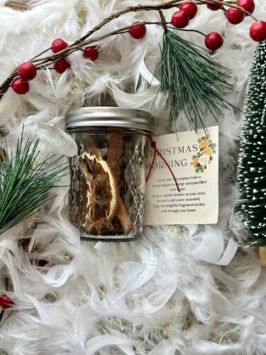 A glass jar filled with dried orange slices, cinnamon sticks, and a label reading 'Christmas Morning,' arranged on a festive background with greenery and decorative elements.
