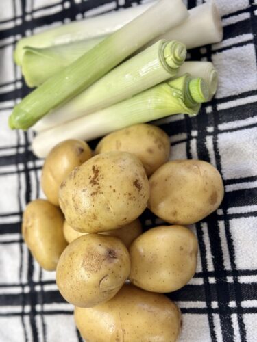 A pile of Yukon gold potatoes and fresh leeks placed on a black and white checkered cloth.