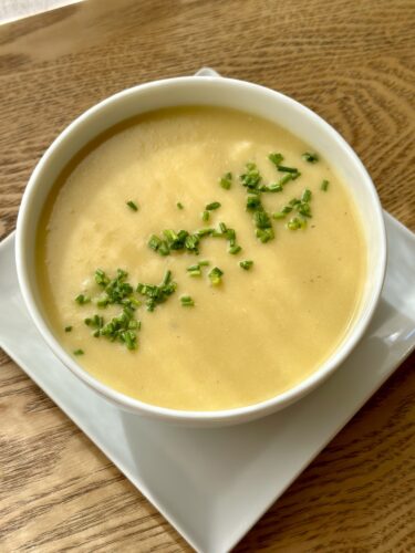 A bowl of creamy soup topped with chopped chives, served on a square white plate.