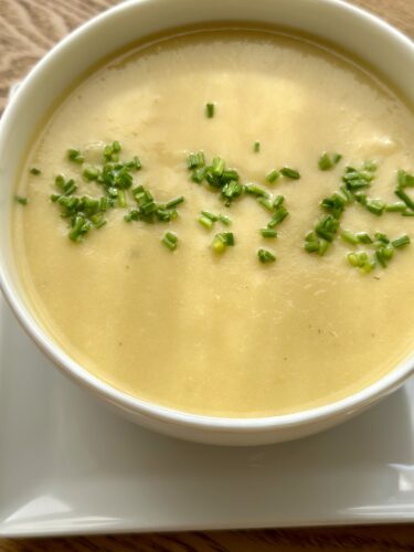 A creamy vegan potato leek soup garnished with fresh chopped chives in a white bowl.