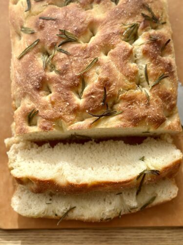 A freshly baked loaf of focaccia topped with rosemary, sliced to reveal its fluffy interior.