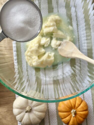A mixing bowl with softened butter, sugar, and a wooden spoon, surrounded by small decorative pumpkins.