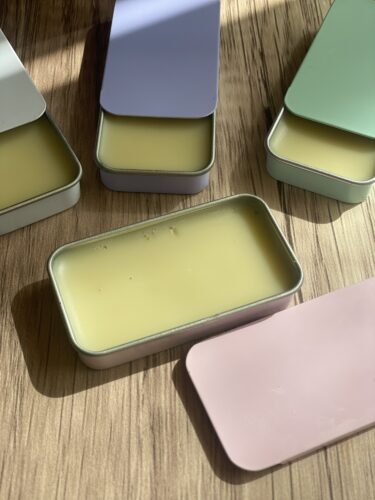Several colorful tins filled with yellow beeswax lip balm arranged on a wooden surface.