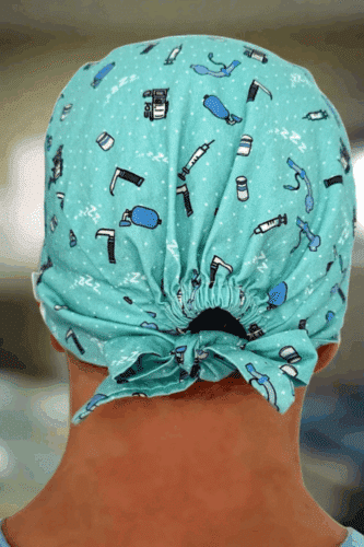 A healthcare worker's head wearing a fun scrub cap featuring various medical tools and equipment designs.