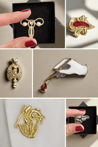 A collection of anatomical-themed enamel pins showcased in a variety of designs, including a uterus, heart, lungs, and hand, with a hand holding one of the pins for display.