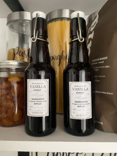 Two dark amber bottles labeled 'Vanilla Extract' in a kitchen shelf with spaghetti jars and a bag of coffee.