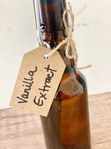 A dark amber glass bottle of homemade vanilla extract with a tag that reads 'Vanilla Extract', tied with twine.