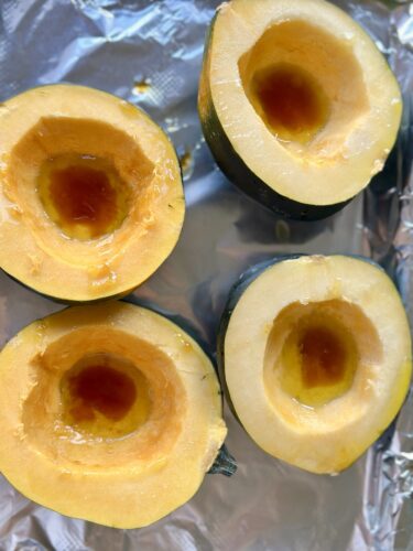 Four halved acorn squashes placed cut-side up on a baking sheet, ready for roasting.