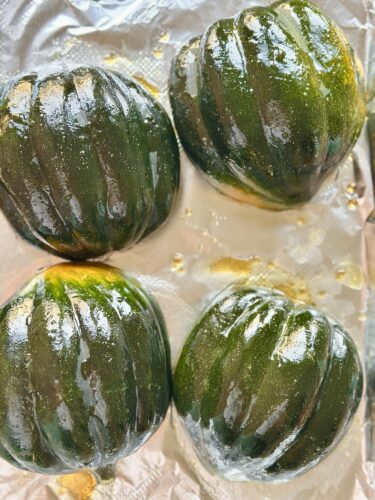 Four halved acorn squash brushed with olive oil and prepared for roasting on foil.