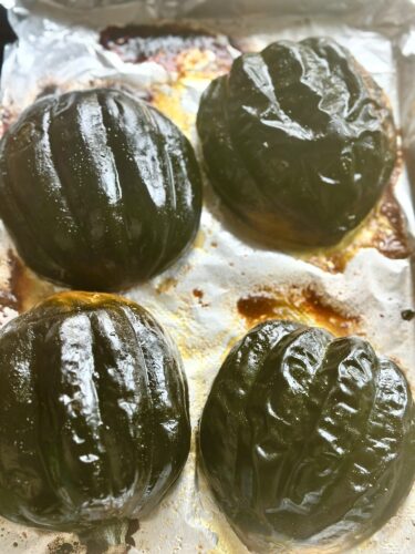 Four roasted acorn squash halves on a baking sheet, lightly caramelized with a golden glaze.