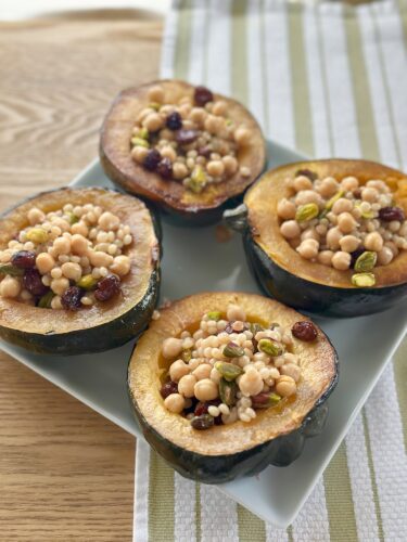 Stuffed acorn squash halves filled with pumpkin pie spice couscous, chickpeas, pistachios, and cranberries, served on a white plate.