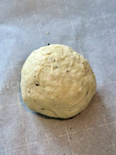 A round ball of dough resting on parchment paper, speckled with seasoning.
