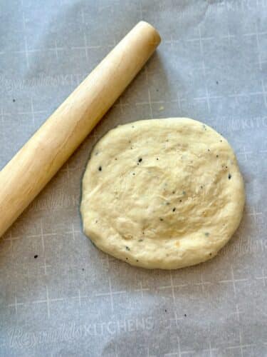 A rolling pin next to a round piece of dough on parchment paper, ready to be rolled out for homemade everything bagel crackers.