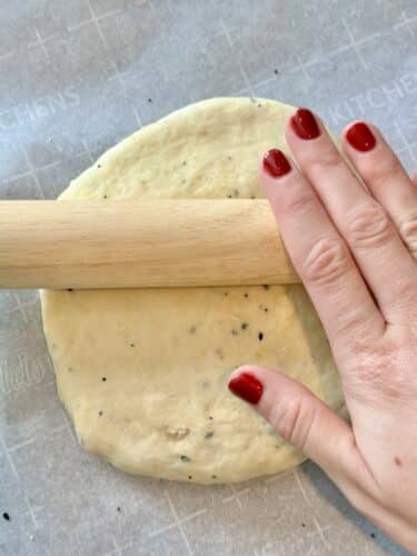 A hand rolling out dough for homemade everything bagel crackers on parchment paper.