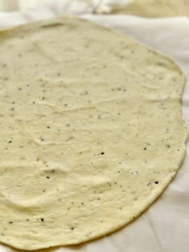 A thinly rolled dough for homemade everything bagel crackers, speckled with seasoning on a piece of parchment paper.