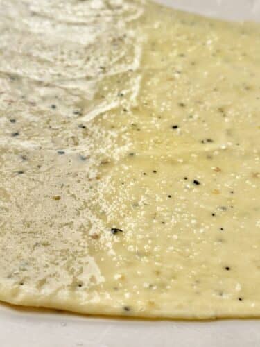 Close-up image of rolled out cracker dough with visible seasoning specks, ready to be baked.