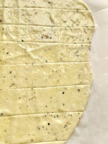 Rolled dough for homemade everything bagel crackers, cut into strips on parchment paper.