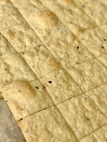 Close-up of baked homemade crackers, scored into squares with a light golden color and sprinkled with seasoning.