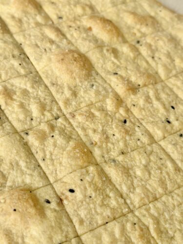 Close-up view of baked everything bagel crackers, scored into squares, showing a textured surface with seasoning flecks.