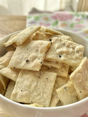 A bowl filled with homemade everything bagel crackers, showcasing their crisp, golden texture and scattered black seeds.