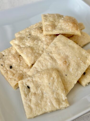 A plate of freshly baked homemade everything bagel crackers, showcasing a golden-brown and crispy texture with visible seasoning flecks.