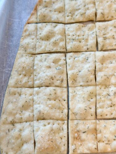 Baked homemade dill crackers cut into squares, resting on a parchment-lined baking sheet.