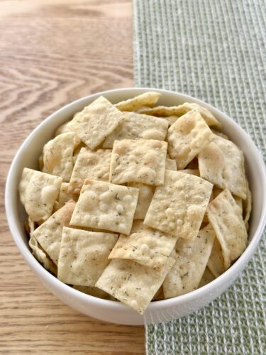 A bowl filled with homemade dill crackers placed on a wooden surface.