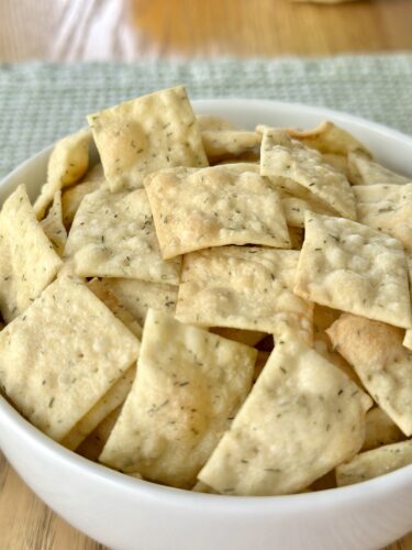 A white bowl filled with homemade dill crackers, showcasing their crispy, golden appearance with visible flecks of dill.