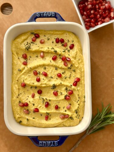 A serving dish filled with whipped feta pumpkin dip, garnished with pomegranate seeds and chopped rosemary.
