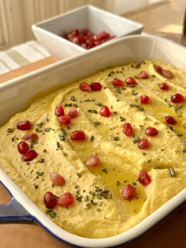 A creamy whipped feta pumpkin dip topped with vibrant pomegranate seeds and fresh rosemary served in a blue baking dish.