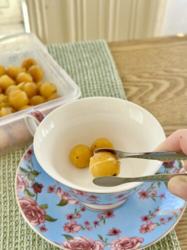 A person using tweezers to pick up frozen yellow immunity cubes from a container, placed in a white cup on a decorative blue plate with flowers.