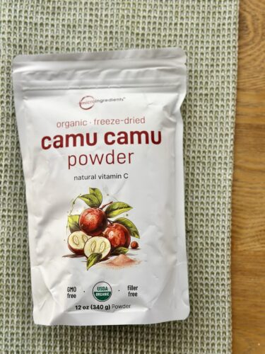 A package of organic freeze-dried camu camu powder, labeled as a natural vitamin C source, placed on a textured green background.