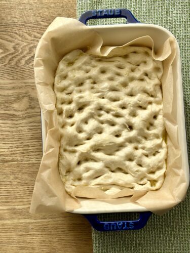 An unbaked flatbread dough resting in a baking dish lined with parchment paper.