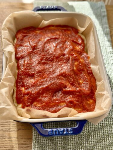 A rectangular baking dish lined with parchment paper, filled with a layer of red sauce.