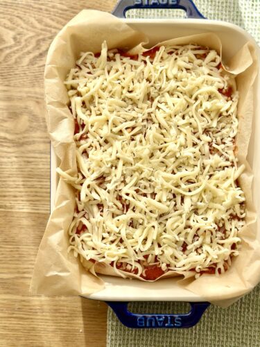 A baking dish filled with lasagna layers topped with shredded mozzarella cheese, ready to be baked.