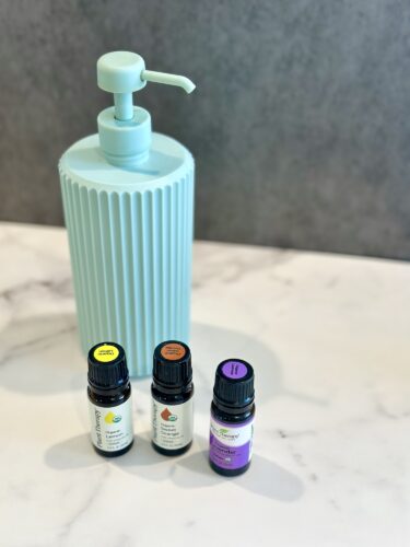 A mint green pump bottle with ribbed design next to three small essential oil bottles on a marble surface.