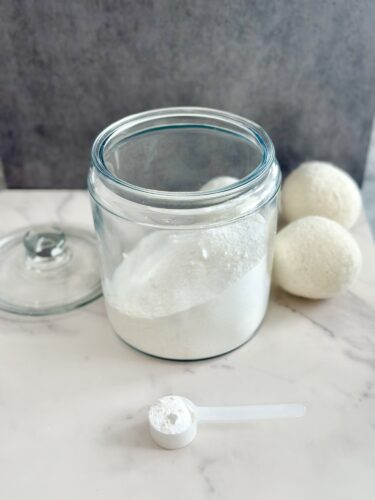 A glass jar filled with white powder, a measuring scoop beside it, and three white round objects in the background.
