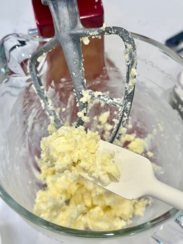 Close-up of a mixing bowl with creamed butter and sugar, featuring a spatula and mixer attachments.