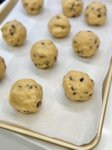 Raw cookie dough balls with chocolate chips arranged on a baking sheet lined with parchment paper.