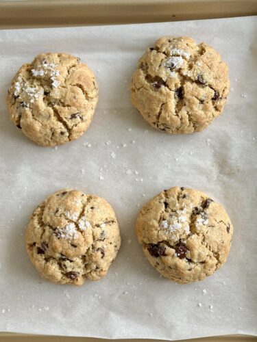 Freshly baked cookies with chocolate chunks sprinkled with coarse salt on parchment paper.